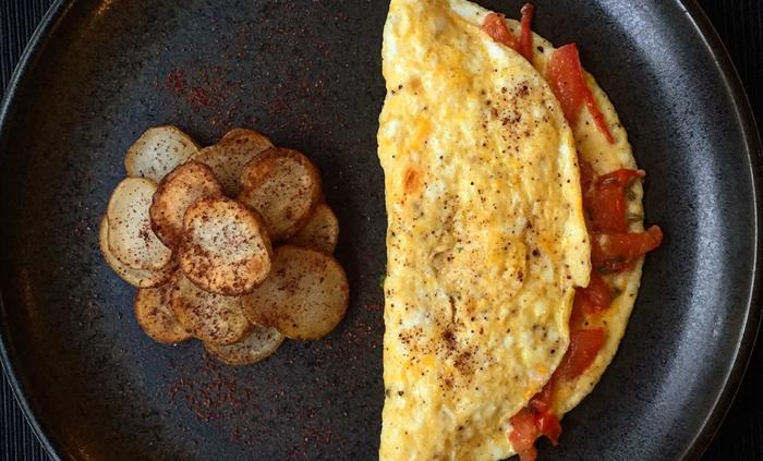 An omelette on a black plate next to a small pile of potatoes